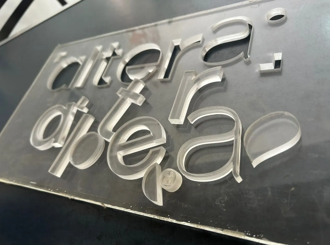 Letras de acrílico transparente de gran espesor recién cortadas, sobre la placa de la que salieron