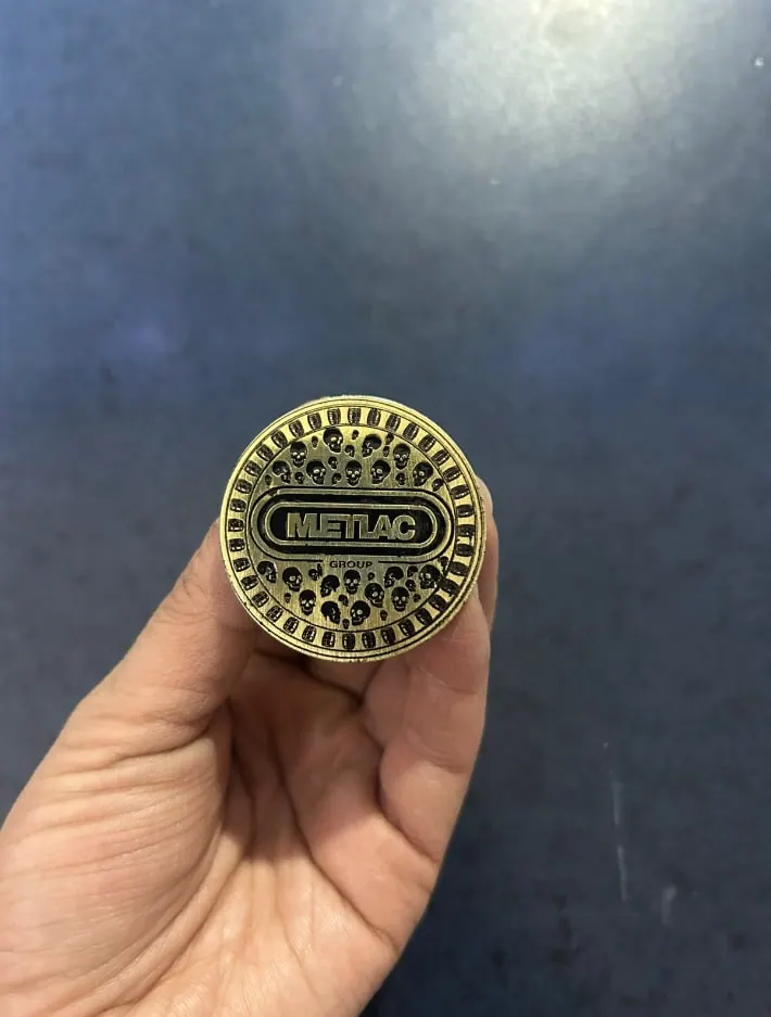 Medalla metálica con logotipo en relieve, sostenida en la mano
