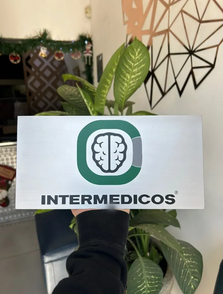 Placa blanca con logotipo verde, sostenida frente a una planta